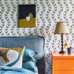 a bedroom with a blue bed, yellow nightstand and colorful wallpaper