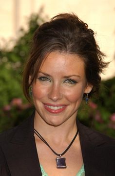 a woman smiling and wearing a necklace with a square shaped pendant on it's neck