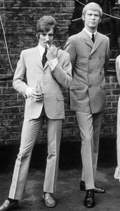 three people standing next to each other in front of a brick wall wearing suits and ties