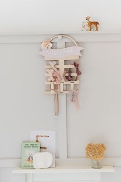 a white shelf topped with a wooden sign and flowers next to a vase filled with flowers