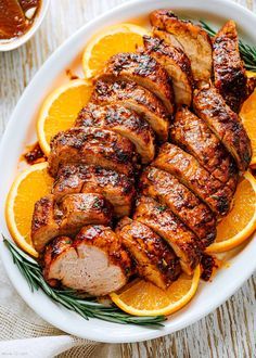 sliced pork and oranges in a white bowl with rosemary garnish on the side