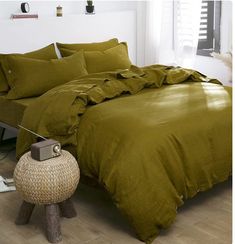 a bed with green sheets and pillows in a room next to a lamp on the floor