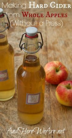 two bottles of apple cider sitting on top of a wooden table next to apples