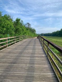 a wooden bridge over a river surrounded by green grass and trees on a sunny day