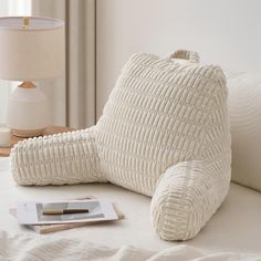 a white teddy bear pillow sitting on top of a bed next to a book and lamp