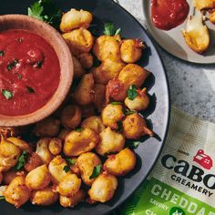 a black plate topped with tater tots next to a bowl of sauce