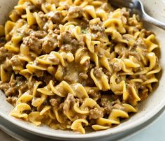 a white bowl filled with pasta and meat on top of a marble table next to a fork