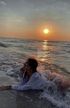 a woman laying on the beach with her feet in the water and sun setting behind her