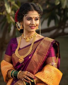 a woman in a purple and yellow sari with gold jewelry on her head is smiling