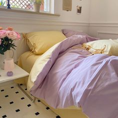 a bed with yellow and purple sheets in a room next to a table filled with flowers