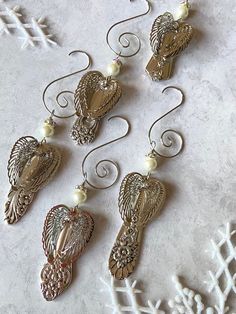 six angel wings with pearls hanging from hooks on a white background, surrounded by snowflakes