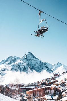 two people riding skis on top of a snow covered slope next to a town