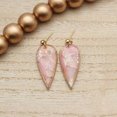 the pink and gold earrings are sitting on a wooden table