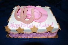 a birthday cake with pink frosting and gold stars on the bottom, sitting on a table