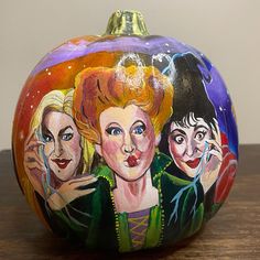 a painted pumpkin sitting on top of a wooden table next to a painting of three women