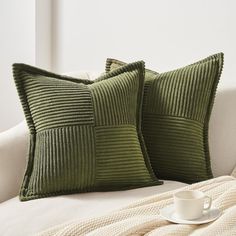 two green pillows sitting on top of a couch next to a cup and saucer