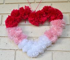 a heart shaped wreath hanging on a brick wall with pom - poms in the shape of a red, white and pink heart