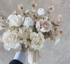 a person holding a bouquet of white and pink flowers in their left hand, against a gray background