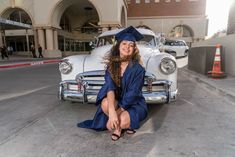 a woman sitting on the ground in front of a car wearing a graduation cap and gown