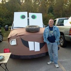 a man standing next to a fake car made out of cardboard boxes with googly eyes