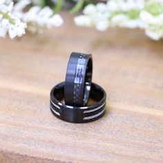 two black rings sitting next to each other on top of a wooden table with flowers in the background