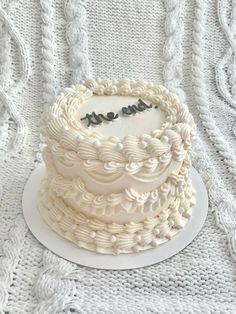 a white cake sitting on top of a plate covered in frosting next to a knitted blanket