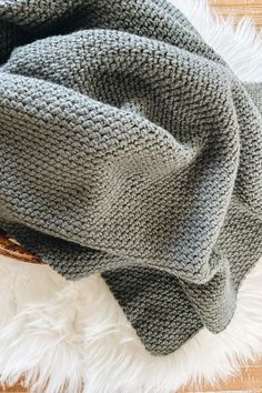 a gray knitted blanket laying on top of a white fluffy rug next to a wooden floor