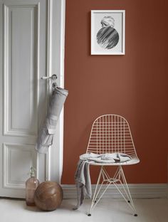 an orange wall in a room with a white chair and vases on the floor