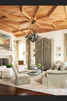 a living room filled with furniture and a chandelier hanging from the wooden ceiling