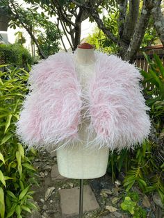 a white mannequin with pink feathers on it's head in front of some bushes