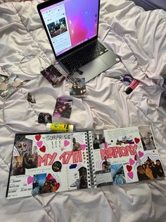 an open laptop computer sitting on top of a white bed covered in pictures and papers