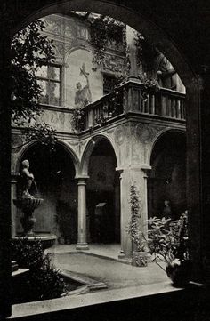 black and white photograph of an old building with statues on the balcony, in front of a fountain