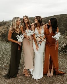 four women in dresses standing together and smiling at each other with flowers on their bouquets