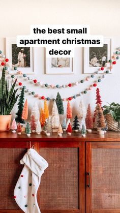 the best small apartment christmas decor is on display in front of a wooden cabinet with stockings and potted plants