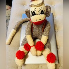 a sock monkey sitting on top of a white chair with red pom poms