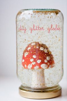 a red and white mushroom in a glass jar with words diy glitter glob