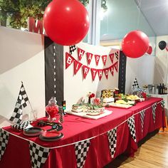 a red table topped with lots of food and balloons in the shape of checkered flags