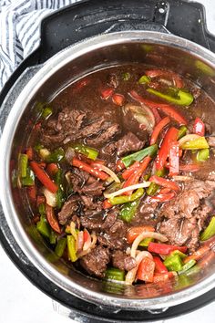 a pot filled with beef and peppers on top of a stove burner next to a towel