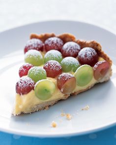 a piece of fruit pie on a white plate with powdered sugar and grapes in the middle