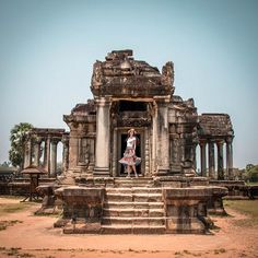 a woman standing in the doorway of an old building with stone columns and steps leading up to it