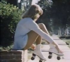 a woman is sitting on the sidewalk with her skateboard