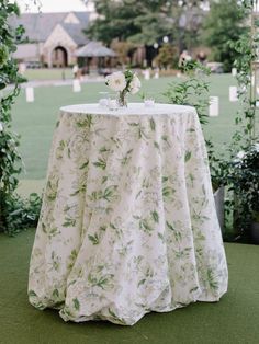 a table with a white cloth and flowers on it in front of greenery at a wedding