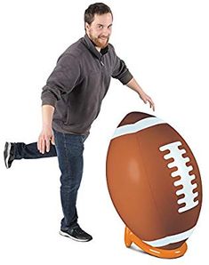 a man standing next to an inflatable football on a white background and pointing at it