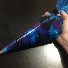 a hand holding a blue plastic cone on top of a black table next to a bag