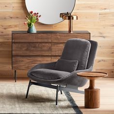 a gray chair sitting in front of a mirror on top of a wooden dresser next to a vase with flowers