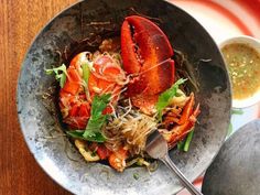 a bowl filled with lobster and noodles on top of a wooden table