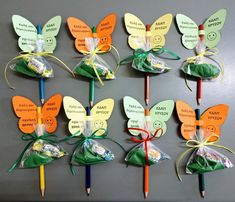 several different colored pencils with butterfly shaped candy wrappers attached to them on a gray surface