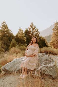 a pregnant woman sitting on top of a large rock in the middle of a field