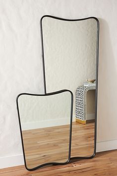 two mirrors sitting on top of a wooden floor next to a white wall with a black frame