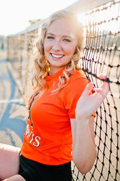 a woman is posing with her tennis racket in front of the net and smiling at the camera